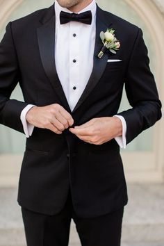 a man in a tuxedo is adjusting his bow tie