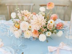 an arrangement of flowers on a blue table cloth with silverware and wineglasses