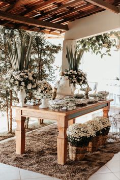 a wooden table topped with lots of white flowers and vases filled with greenery