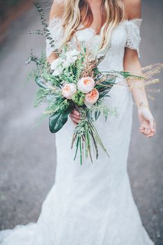 a woman in a white dress holding a bouquet of flowers and greenery on her wedding day