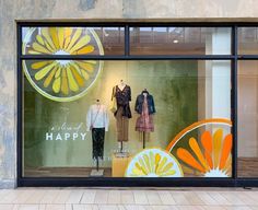 a display window with clothing on mannequins and an orange flower in the background