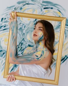 a woman is holding up a painting in front of her face and body with paint all over it