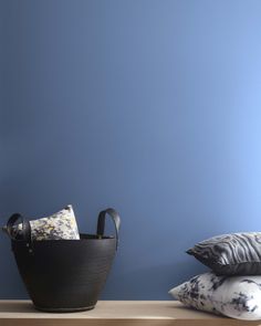 a black basket sitting on top of a wooden table next to pillows and a pillow