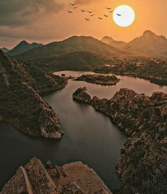 birds flying over a lake surrounded by mountains at sunset in the middle of the day