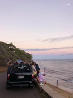 a group of people standing on the side of a road next to water and trees