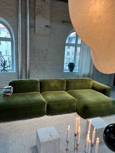 a large green couch sitting in front of two candles on top of a white rug