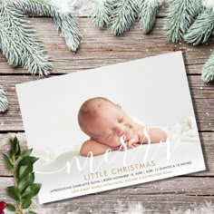 a baby's first christmas card is laying on a wooden surface with pine branches