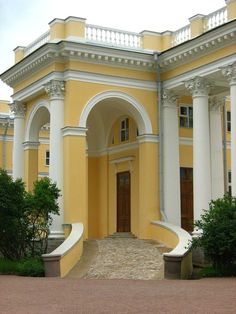 a large yellow building with white columns and arches on the front door, along with steps leading up to it