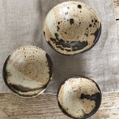 three black and white bowls sitting on top of a wooden table next to a napkin