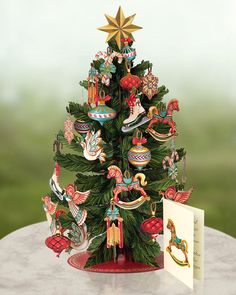 a small christmas tree with ornaments on it next to a greeting card and an ornament