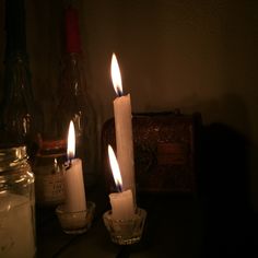 three lit candles sitting on top of a table next to a bottle and glass container