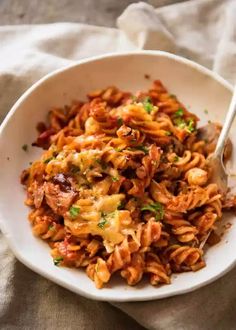 a white bowl filled with pasta covered in sauce and parsley on top of a table