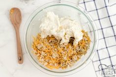 a bowl filled with cheese and other ingredients next to a wooden spoon on a white counter