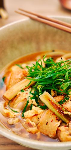 a bowl filled with meat and vegetables on top of a wooden table next to chopsticks