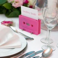 there is a pink cassette on the table with silverware and wine glasses next to it