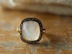 a gold ring with a white stone surrounded by black diamonds on a wooden surface in front of a couch