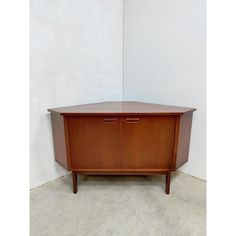 a wooden cabinet sitting on top of a cement floor next to a wall with a white background