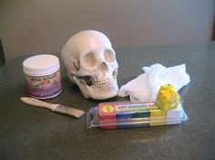 a skull sitting on top of a counter next to some paint and a toothbrush