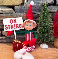 an elf is sitting next to a sign that says on strike