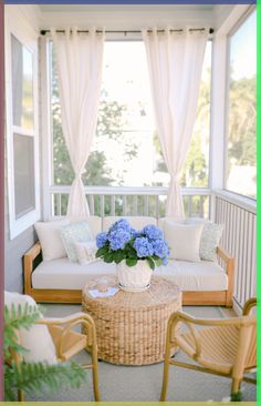 a living room filled with furniture and blue flowers on top of a table in front of a window