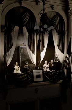 an old photo of some people sitting at a table in a room with curtains on the walls