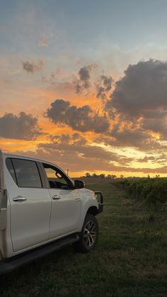 a white truck parked on top of a lush green field under a cloudy sky at sunset