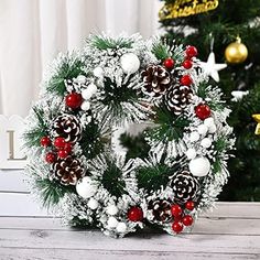 a christmas wreath with pine cones and red berries is on a table next to a christmas tree