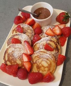 some pancakes and strawberries on a white plate with chocolate dipping in the middle for toppings