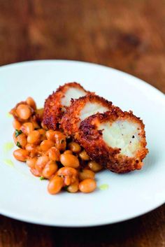 a white plate topped with meat covered in sauce and garnished with chickpeas