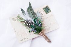 a piece of paper with feathers and flowers on it sitting on top of a white sheet