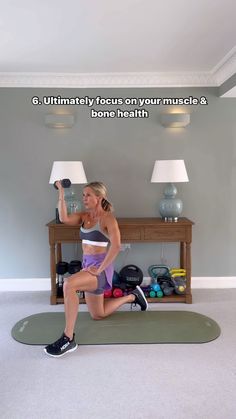 a woman doing squats on a mat in front of a table with a lamp