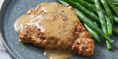 meat with gravy and green beans are on a blue plate, ready to be eaten