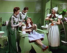 three women and two men in green dresses are washing dishes while one woman is holding a cat