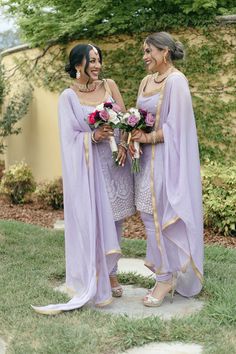 two women standing next to each other wearing purple outfits and holding flowers in their hands