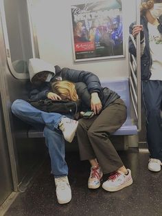 two people sleeping on a subway train next to each other with their heads resting against one another