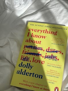 a yellow book sitting on top of a bed next to a white comforter with the words everything i know about friends, dads, love and dolly alderon