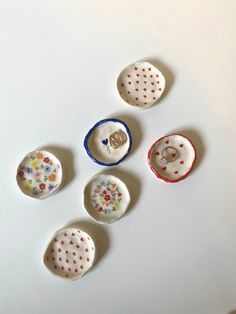 five ceramic buttons with designs on them sitting on a white counter top next to a pair of scissors