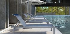 lounge chairs and an umbrella are lined up by the pool