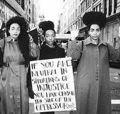 black and white photograph of three women holding protest signs in the middle of an urban street