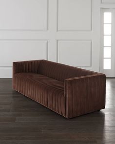 a red velvet couch sitting on top of a hard wood floor next to a white wall