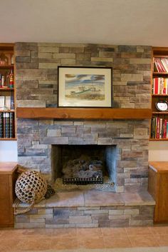 a stone fireplace in a living room with bookshelves on either side and a painting above it