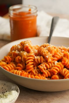 a white bowl filled with pasta and sauce next to a jar of seasoning on the table