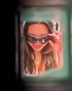 a woman wearing sunglasses looking through a mirror