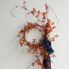 a wreath with berries and a blue bow hanging on the wall next to a white wall