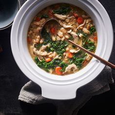 a white bowl filled with chicken and vegetable soup next to a wooden spoon on top of a table