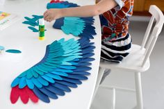 a young boy is painting an angel wing on a white table with blue and red wings