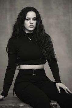 a woman sitting on top of a wooden bench wearing black pants and a cropped shirt