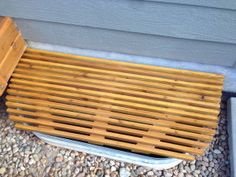 a wooden bench sitting on top of gravel next to a wall and window sill