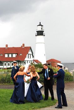 a group of people standing around each other in front of a light house and water