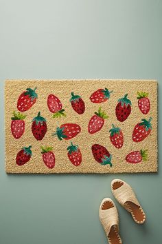 a pair of shoes sitting on top of a rug next to a door mat with strawberries